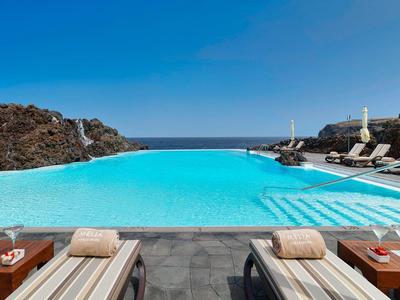 Basen infinity z leżakami na czarnej kamiennej platformie z widokiem na morze pod czystym niebem.