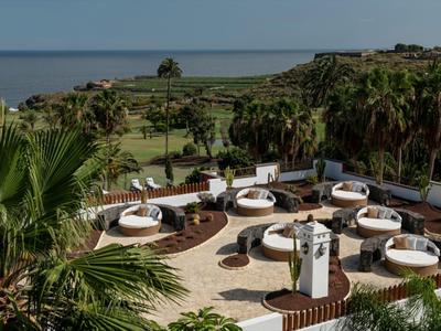 Terrace with round white sunbeds overlooking garden and sea under clear sky.