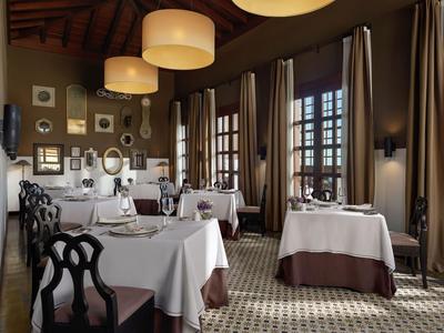 Elegant restaurant with white tablecloths, wooden chairs, and warm lighting in a room with tall windows.