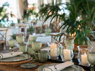 Elegant dining table in restaurant with candles, glasses, and decorative plants in the background.