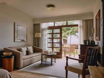 Cozy hotel room with sofa, armchair, and balcony overlooking greenery.