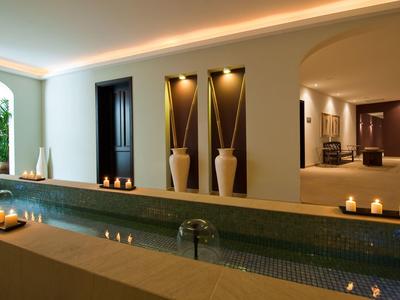 Nowoczesna strefa wellness z basenem wewnętrznym, łagodnym oświetleniem i dekoracyjnymi wazonami na ścianie.