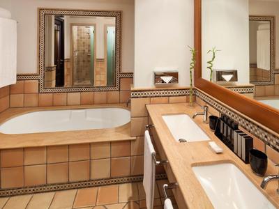 Elegancka łazienka z wanną, podwójnymi umywalkami i dużymi lustrami w ciepłych odcieniach ziemi.