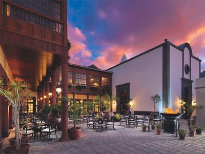 Dziedziniec hotelowy z krzesłami, stolikami i dekoracyjnym ogniem o zachodzie słońca.