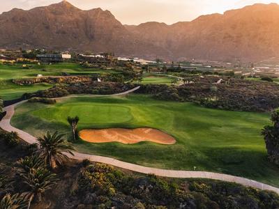 Pole golfowe z bunkrem piaskowym przed górami o zachodzie słońca.