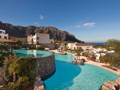 Duży basen w hotelu z białymi budynkami i górami w tle.