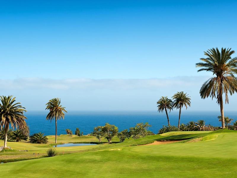 Basen infinity z leżakami na czarnej kamiennej platformie z widokiem na morze pod czystym niebem.