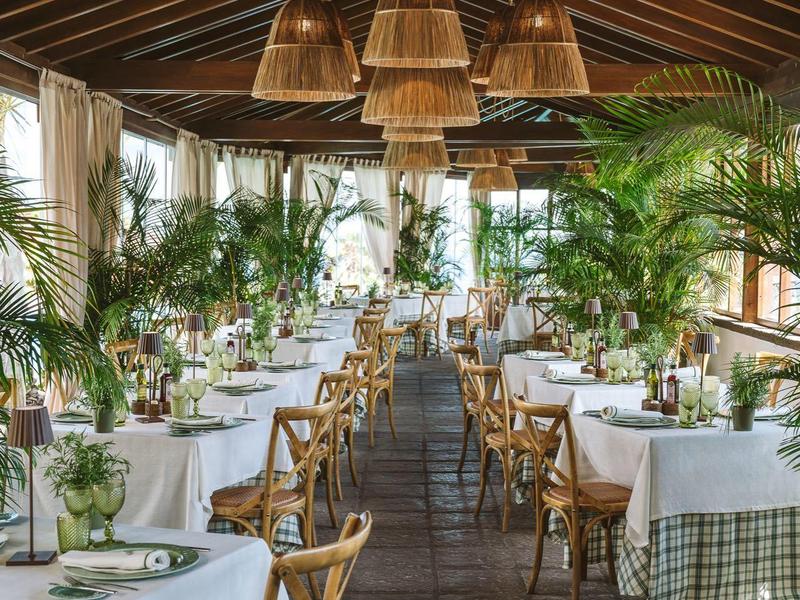 Elegancka jadalnia z rzędami stołów, drewnianymi krzesłami i prostymi lampami z rattanu.