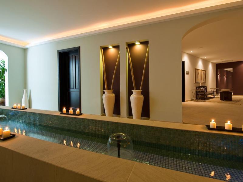 Nowoczesna strefa wellness z basenem wewnętrznym, łagodnym oświetleniem i dekoracyjnymi wazonami na ścianie.