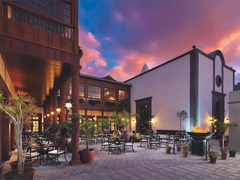 Dziedziniec hotelowy z krzesłami, stolikami i dekoracyjnym ogniem o zachodzie słońca.