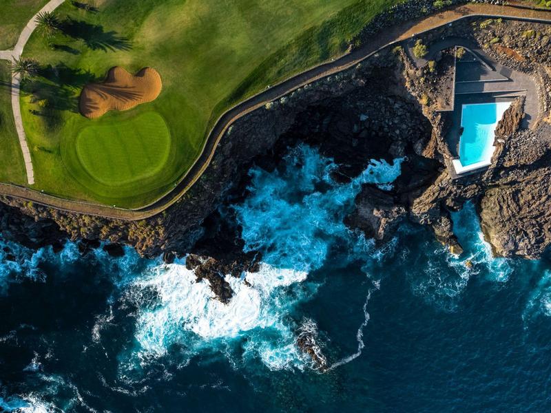 Widok z lotu ptaka na basen na skalistym wybrzeżu obok zielonego pola golfowego.