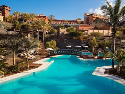 Großer Pool vor einem Resort mit Palmen und Liegestühlen bei Sonnenuntergang.