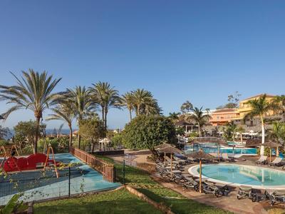 Hotelpoolbereich mit runden Schwimmbecken, Liegestühlen und Palmen unter klarem Himmel