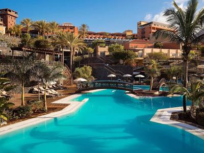 Piscina turchese circondata da palme in un complesso alberghiero soleggiato.