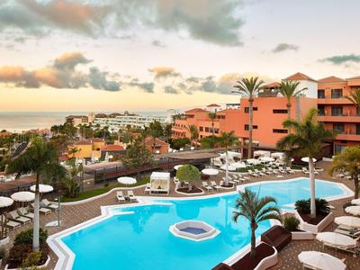 Piscine d'hôtel avec transats et palmiers au coucher du soleil en bord de mer.