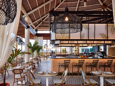 Moderner Hotelbarbereich mit Holzstühlen, großem Tresen und dekorativen Lampen unter einer hohen Holzbalkendecke.