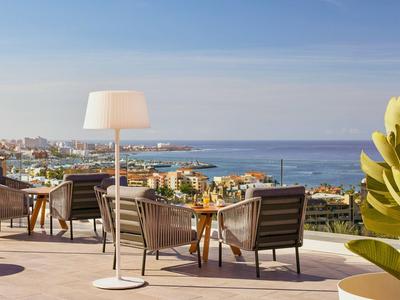 Terrasse mit Sitzmöbeln und Blick auf die Küste und das Meer bei klarem Himmel.