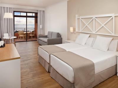 Chambre d'hôtel moderne avec lits jumeaux, canapé, balcon et vue sur la mer.