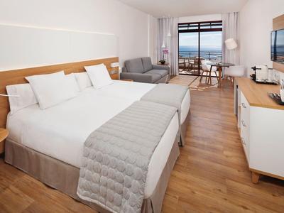 Chambre d'hôtel spacieuse avec deux lits, terrasse et vue mer.