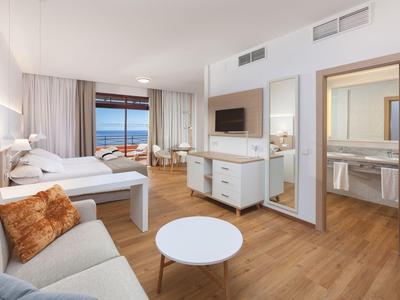Chambre d'hôtel spacieuse avec lit double, canapé, télévision et vue sur la mer.