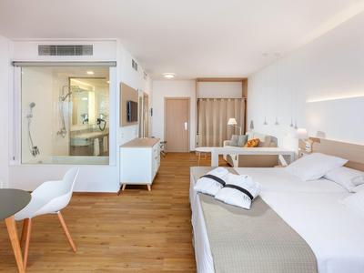 Chambre d'hôtel moderne avec grand lit, parquet et salle de bain vitrée.