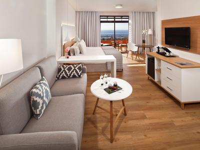 Modern eingerichtetes Hotelzimmer mit Sofa, Bett, Flachbildschirm und Meerblick.