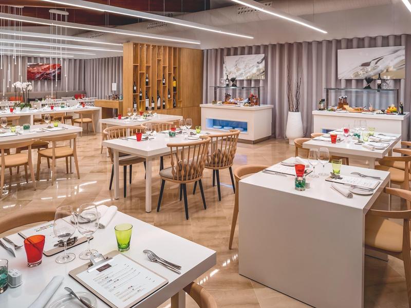 Salle de restaurant moderne avec tables dressées, chaises en bois et décorations élégantes.