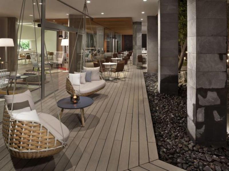 Elegantní venkovní lounge s závěsnými křesly a nízkými stoly na dřevěné terase.