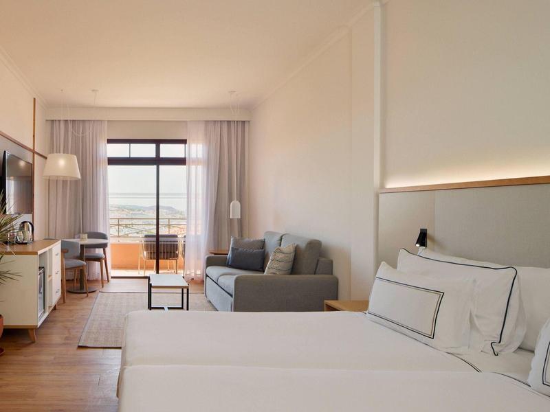 Chambre d'hôtel lumineuse avec lit double, canapé, balcon et vue dégagée.