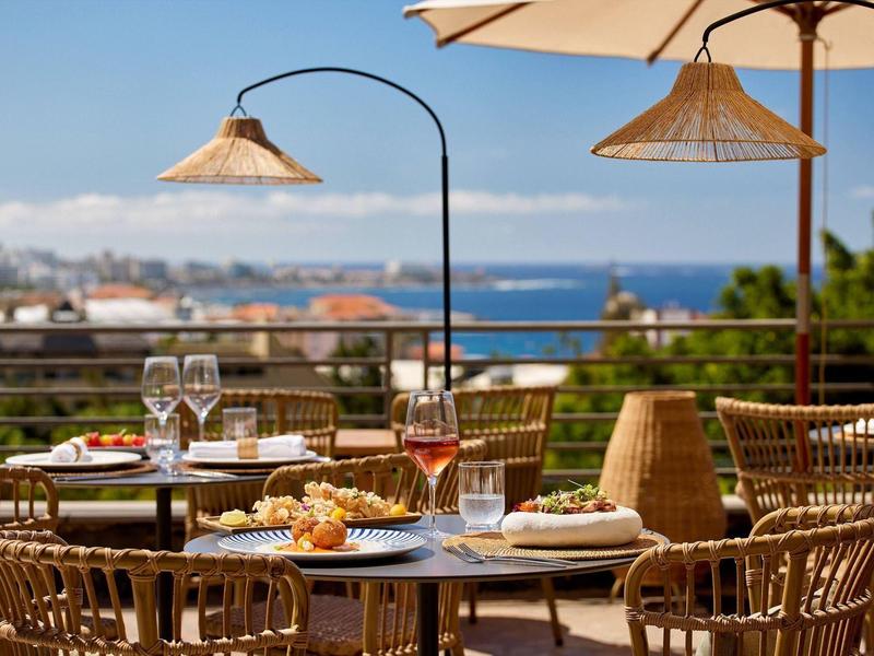 Vue d'une terrasse de restaurant avec tables dressées et vue sur la mer.