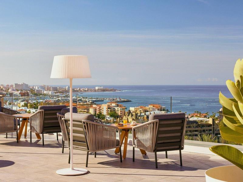 Terasa s židlemi a lampou s výhledem na moře a střechy.