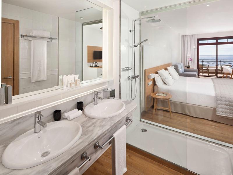 Salle de bain moderne avec double lavabo et baignoire donnant sur chambre lumineuse avec balcon.