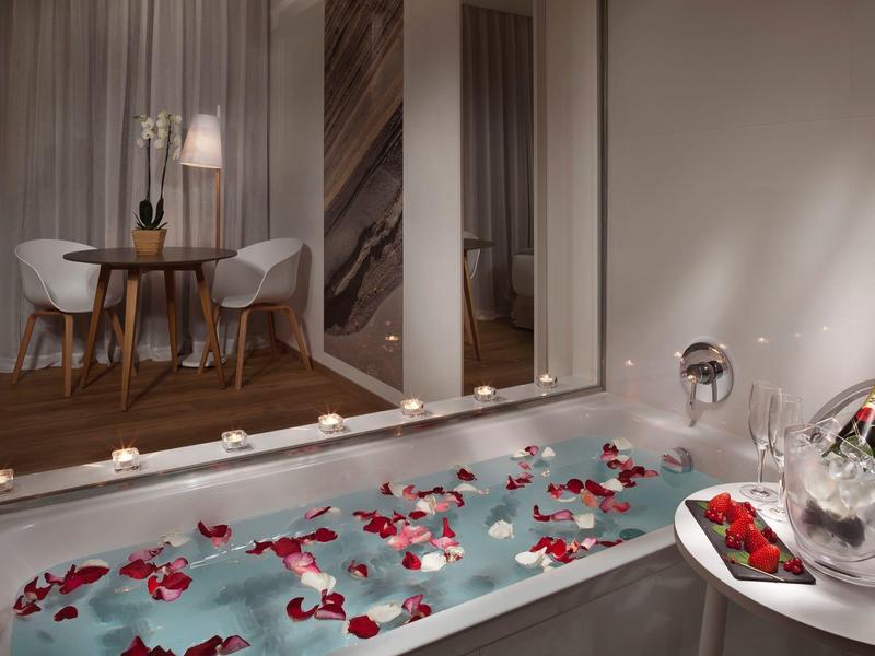 Vana s okvětními lístky, šampaňským a růžemi, romantická a intimní atmosféra v hotelovém pokoji.