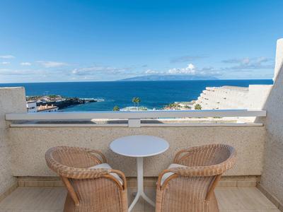 Terrasse mit zwei Korbstühlen und kleinem weißen Tisch, Blick auf blaues Meer und Himmel.