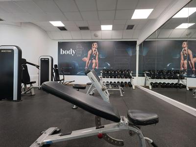 Nowoczesna siłownia z ławką do ćwiczeń, lustrzaną ścianą i sprzętem treningowym.
