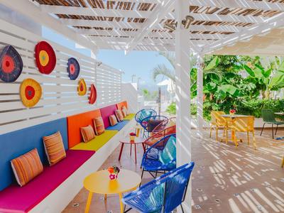 Kolorowy salon z poduszkami i krzesłami pod pergolą, otoczony roślinami.