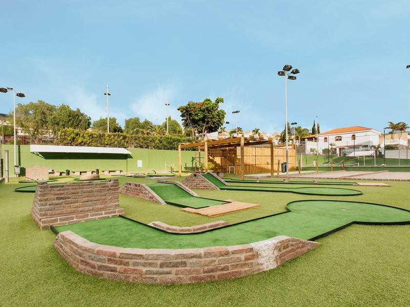 A modern outdoor mini-golf course with green artificial turf and several holes.