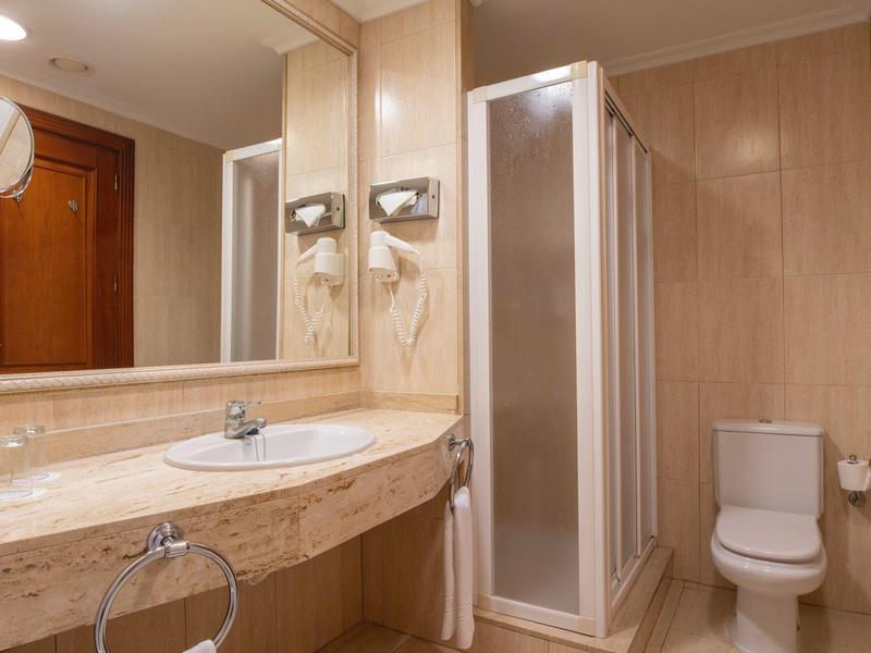Bright bathroom with large mirror, marble sink, shower, and toilet.