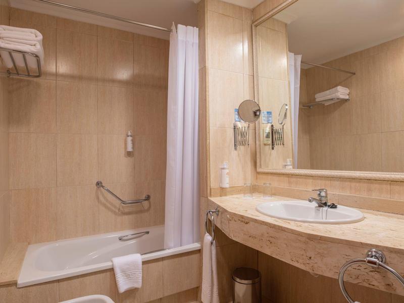 Modern bathroom with bathtub, shower curtain, toilet paper, and sink with large mirror.