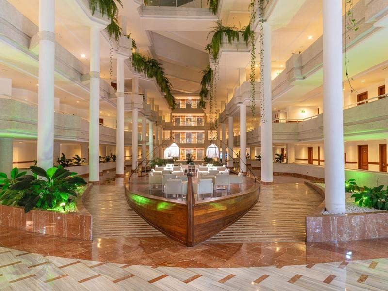 Large hotel lobby with white pillars, plants, and a decorative boat