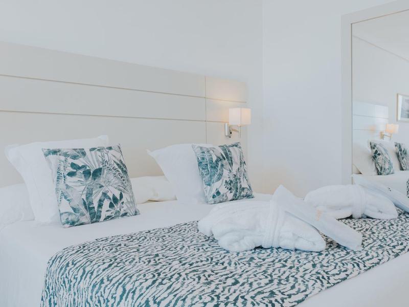 Bright hotel room with double bed, decorative pillows, large mirror, and modern lighting.