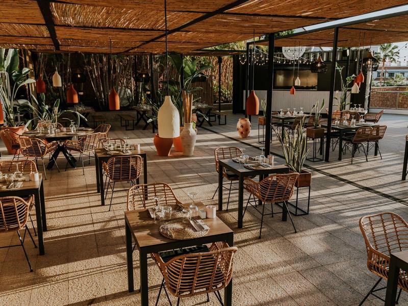 Elegant restaurant with metal chair sets and shaded bamboo roof, surrounded by plants.