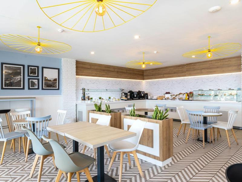 Bright, modern hotel restaurant with white tables, blue chairs, and geometric flooring.