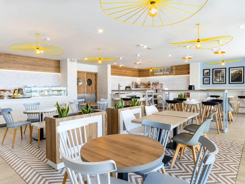 Bright, modern restaurant with round wooden tables and mixed chairs in warm tones.