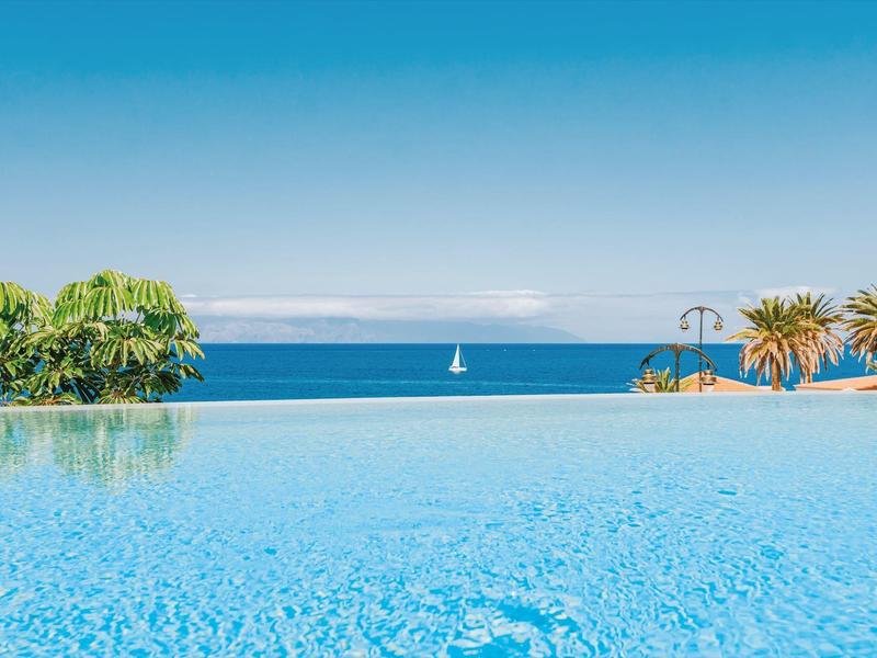Infinity pool overlooking the blue sea with a sailboat on the horizon.