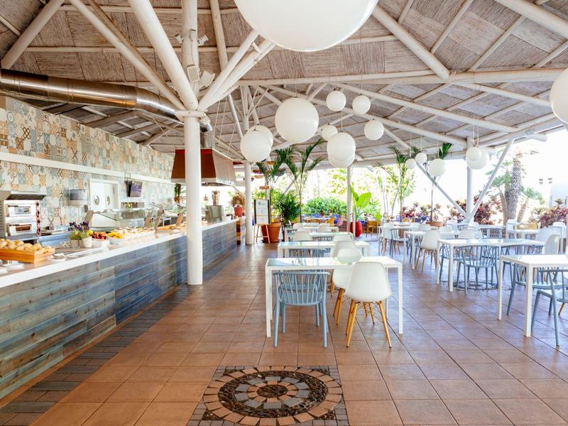 Brightly lit restaurant with white tables and chairs under a structured roof.