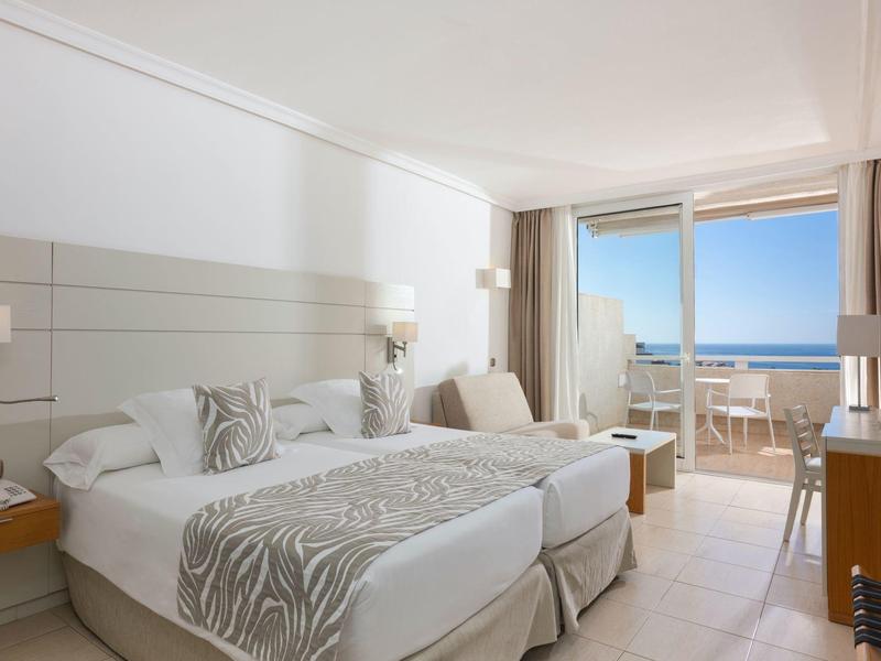 Bright hotel room with two single beds and balcony overlooking the sea.