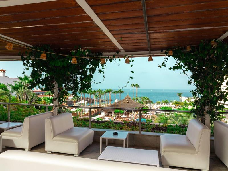 Covered lounge with white sofas and sea view behind green plants