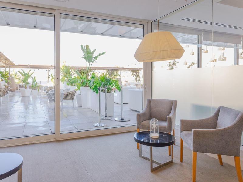 Bright lounge with two armchairs and glass wall overlooking sunny terrace with plants.