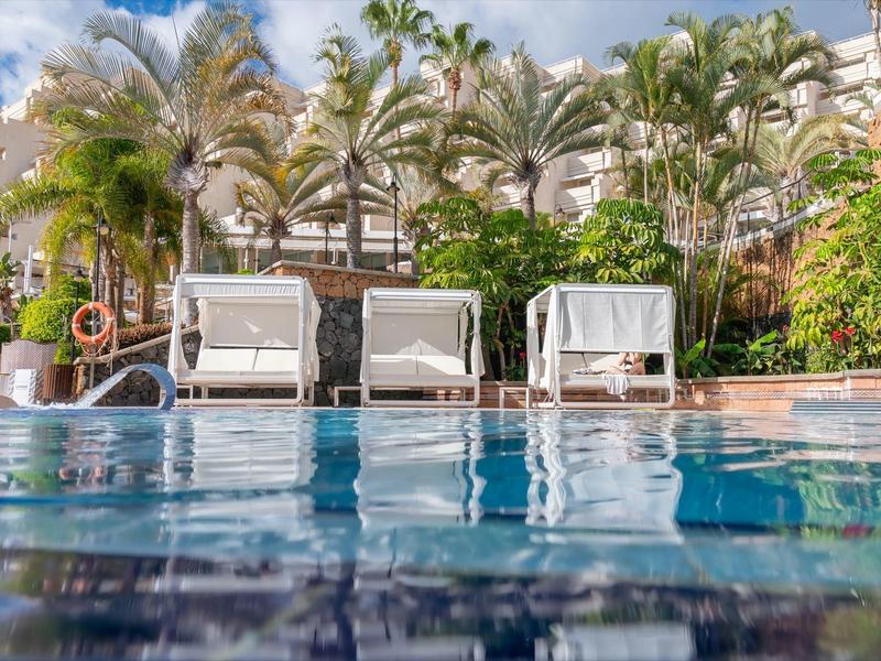Swimming pool with lounge chairs and palm trees in a vacation setting.